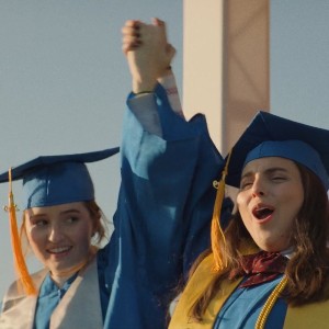 Screenshot from Booksmart, with two best friends wearing graduation caps and gowns and thrusting their clasped hands in the air