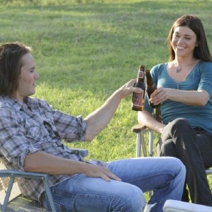 Tim Riggins and Lyla Collette toasting with beers while sitting on chairs outside in Friday Night Lights