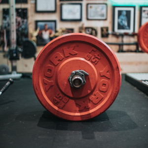 A red barbell weight sits on a black mat