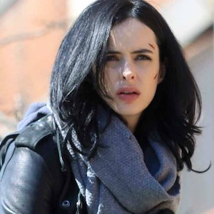 A woman with dark hair (Jessica Jones) looks into the distance with a concerned/confused look on her face