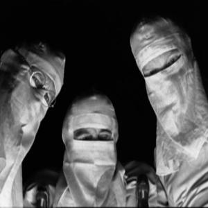 Clip from the movie, Johnny Got his gun. Three black and white figures in old timey surgical masks look down at a patient