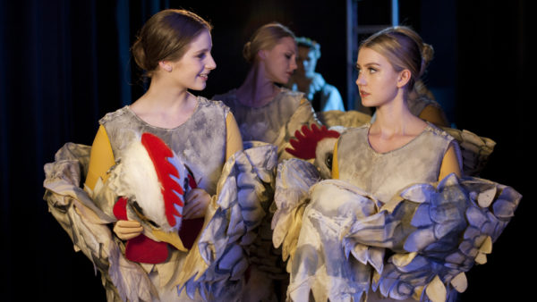 Tara and Grace, wearing chicken costumes and holding the heads, looking at each other