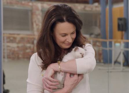 Miss Raine cradling a little white kitten