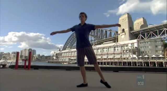 Sam, dancing in front of a big building on the water