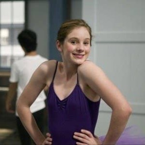 Tara, a brunette, shrugging and smiling in a dance leotard