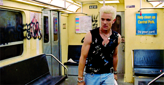 Spike, wielding a metal pole and dressed like Billy Idol (punk black top and spiky bleached hair) as he walks down a subway car