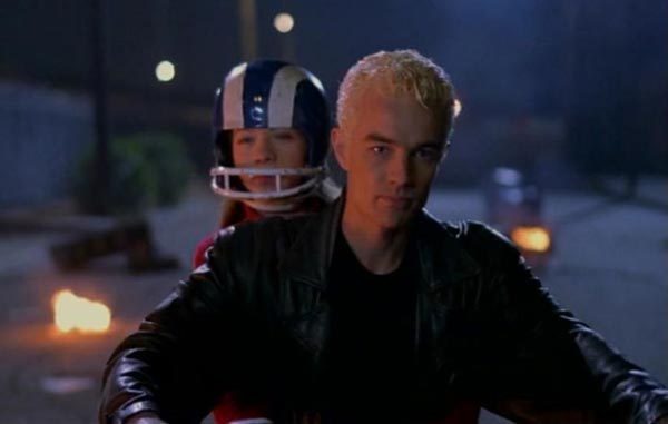 Dawn, wearing a football helmet, riding behind Spike on a motorcycle