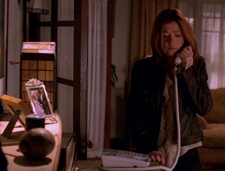 Willow on the phone next to a shelf with a framed photo of a couple