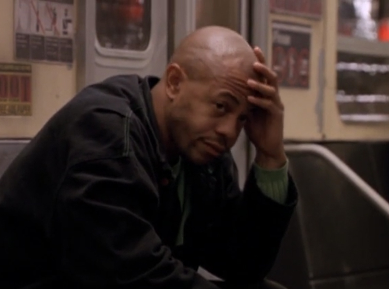 A middle aged Black man, with a shaved head, holding his head in his hand in exasperation