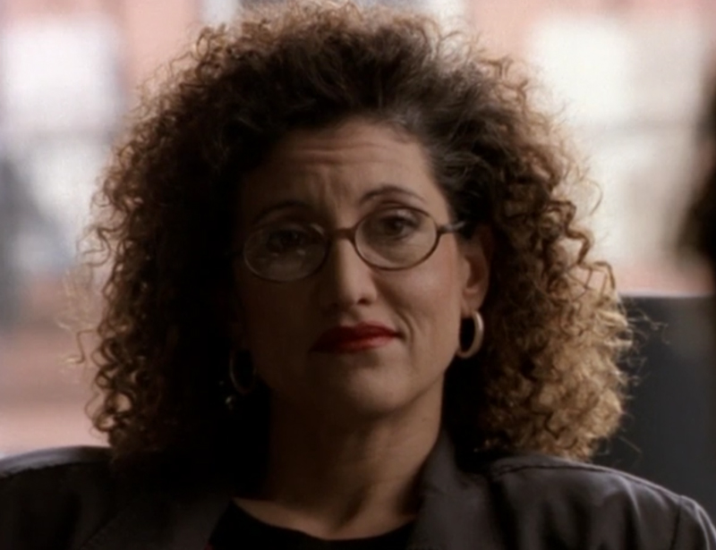 Dr. Pavone, a white woman with curly big brown hair and wearing glasses, played by Amy Aquino