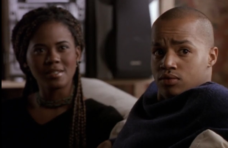 Elena sitting next to Tracy, an attractive Black man with a shaved head, played by Donald Faison