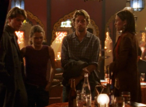 Noel, Felicity, Ben, and Julie standing together and staring at a bottle on the table