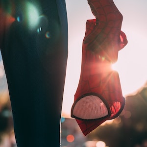 A person holds a Spider-Man mask in front of a setting sun