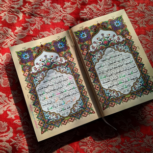 An open Quran with colourful and ornate pages, on top of a red rug with gold floral patterns