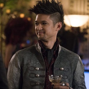 Magnus Bane (Harry Shum Jr.) holding a cocktail and smirking