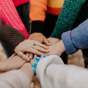 A group of people with colorful sleeves put their hands on top of each other in the middle of a circle