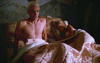 Spike sits up in bed shirtless with a sleeping Buffy next to him.