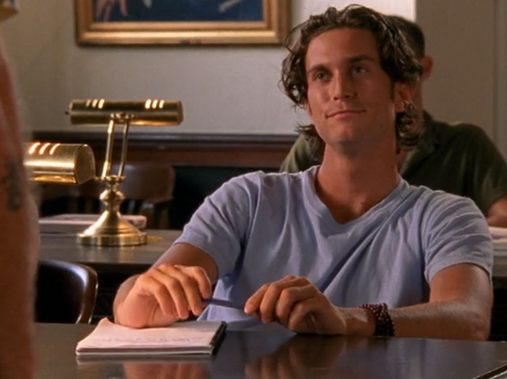 Oliver Hudson sits at a desk looking smug