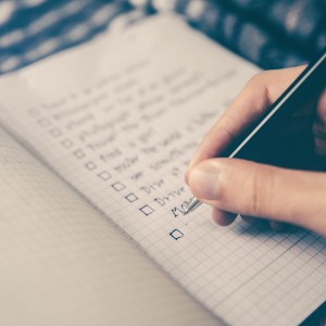 A person's hand, writing a list of items in a notebook with a pen