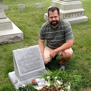 Brian squating next to Lovecraft's simple grave