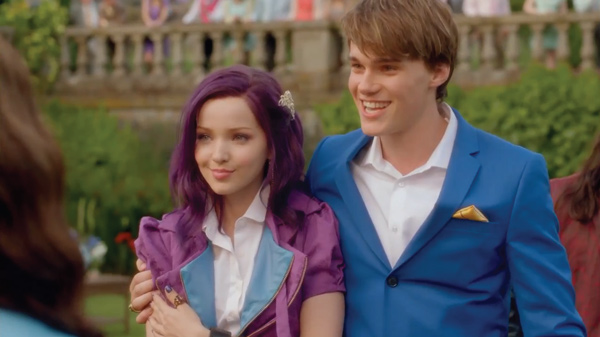 Mal, wearing a purple jacket and smiling, with Ben, wearing a blue suit jacket, who has his arm around her 