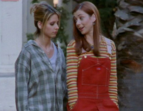 Buffy, wearing a flannel shirt, walking with Willow, who is wearing a red and yellow striped long-sleeved shirt under red overalls