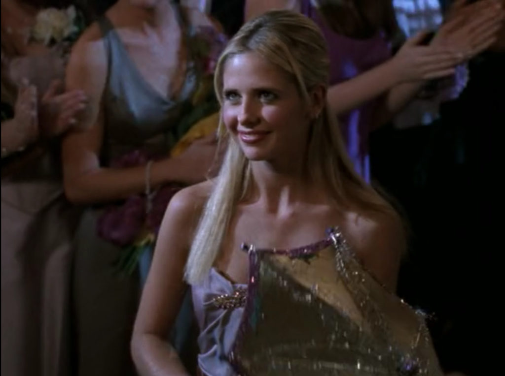 Buffy, smiling and standing in the crowd at prom while holding a glittery parasol