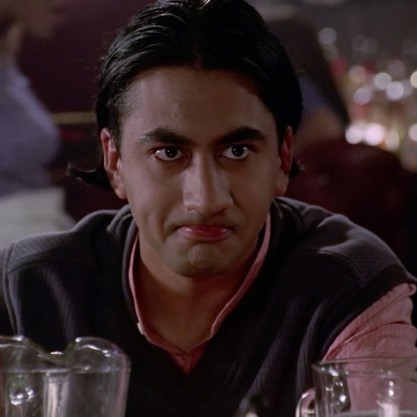 Kal Penn, with slicked back hair, wearing a collared shirt and sweater vest