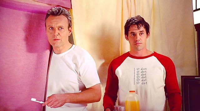 Giles, holding a toothbrush, standing next to Xander, holding a bottle of orange juice