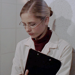 Buffy, with her hair pulled back in a severe bun, wearing glasses and a lab coat