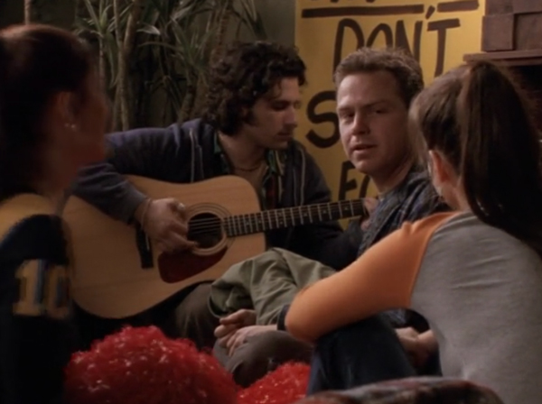 Hal Ozsan as a hippie-looking guy with shaggy hair, playing the guitar