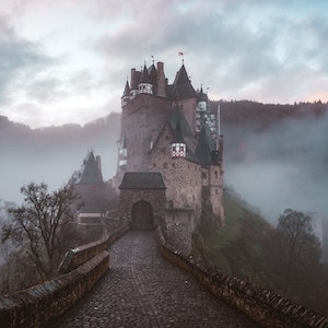 A castle sits at the end of a road surrounded by ominous fog