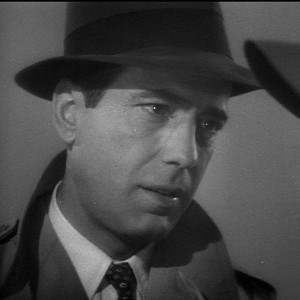 Screenshot from Casablanca of Humphrey Bogart, wearing a fedora, trench coat and tie