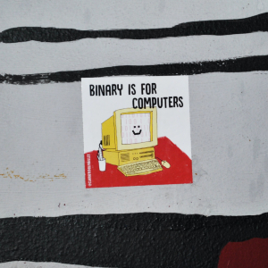 Photo of a table with a sticker on it that says "Binary is for computers" with an illustration of a smiling computer