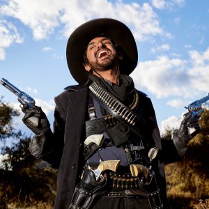 Karan Soni in Miracle Workers: Oregon Trail. Soni, dressed as a cowboy, brandishes multiple guns