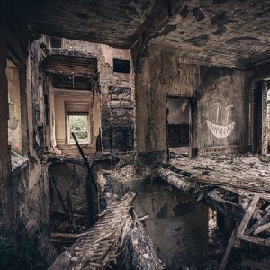 Inside of a big crumbling abandoned stone building with rotted floor and graffiti on the wall