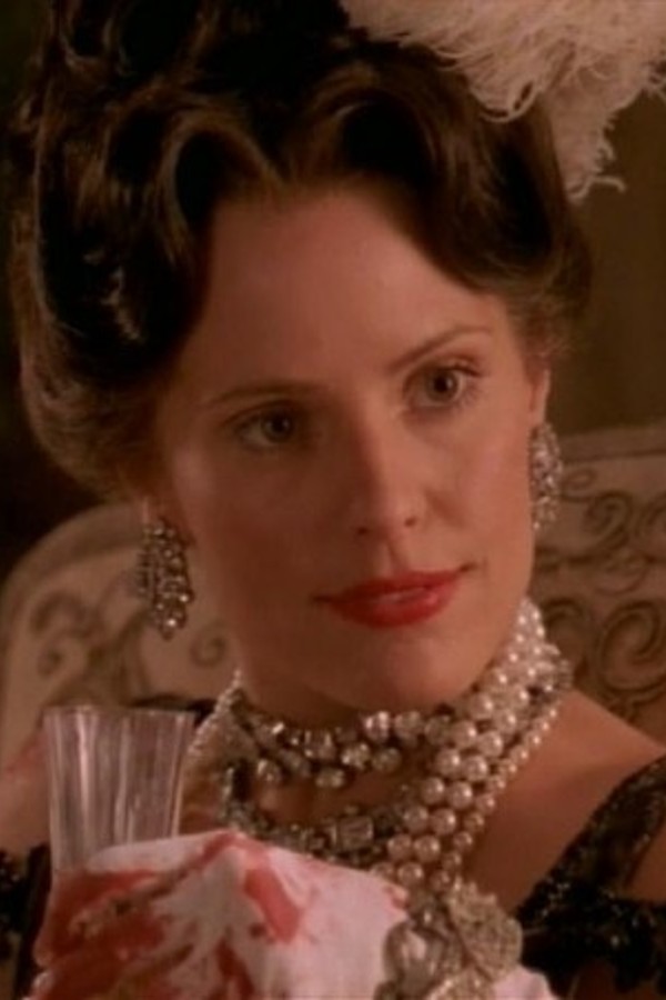 Anya in period costume, gloves, and pearls, holding a champagne flute