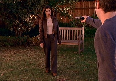 Kennedy wears brown bootcut pants, a tan knit top and a brown bomber-style jacket while in the backyard where Warren shot Buffy