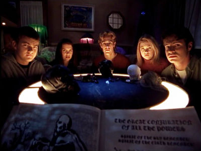The Dawson's Creek gang are lit by candlelight around a table, looking spooked