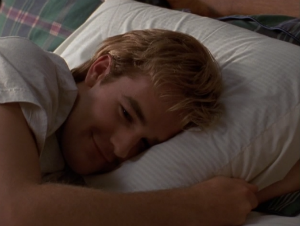 Dawson lies on his side, smiling in bed