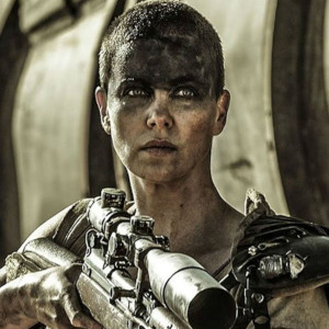 Charlize Theron as Furiosa from Mad Max: Fury Road holds a gun a stares fiercely just off camera