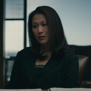 Denise, an Asian American woman with shoulder-length dark hair, wearing a suit