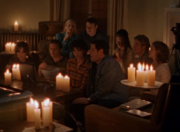 The entire crew sitting in a dark apartment with candles as their only light