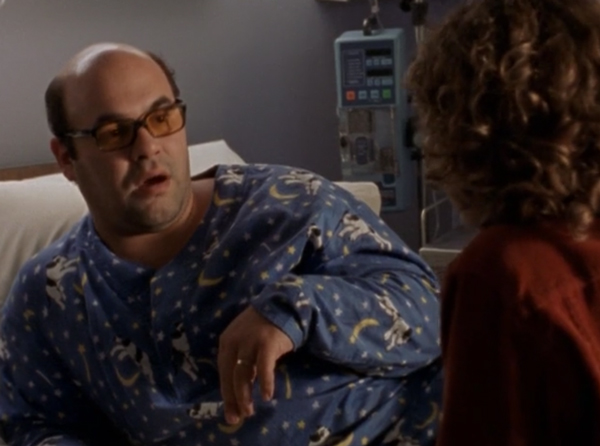 Javier, lounging in a hospital bed and wearing blue long-sleeved pajamas with a print of cows jumping over moons