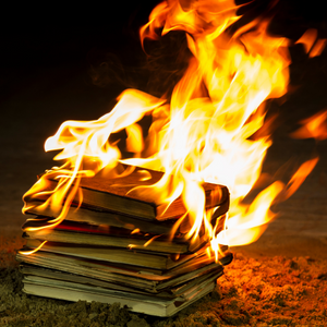 A pile of books sitting in the sand, on fire.