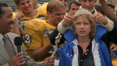 Jen, surrounded by an adoring crowd, is being crowned homecoming queen on the football field while she has a confused and unhappy look on her face