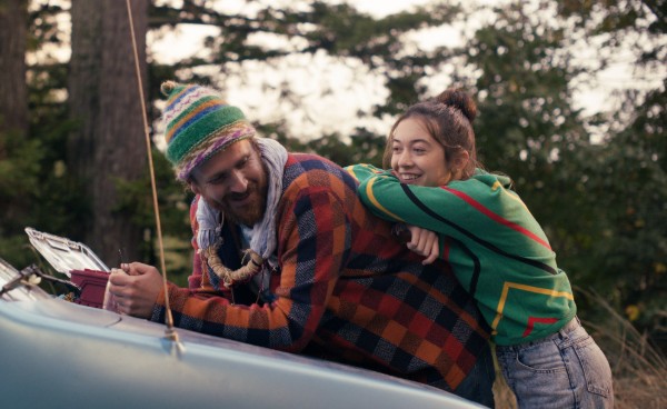 Big leaning on the hood of the Truthmobile while Lennie, smiling, leans on him