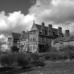 A B&W image of a large mansion or estate with bare bushes on the lawn