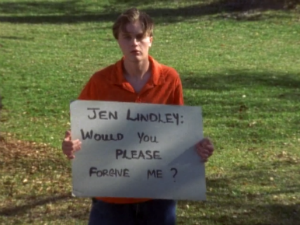 Henry stands in Jen's yard looking pitiful and holding a sign that reads "JEN LINDLEY WOULD YOU PLEASE FORGIVE ME?"