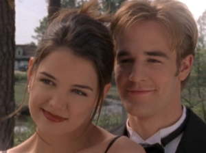 Joey and Dawson pose for a picture in his front yard. She's in a pretty black strappy dress with her hair up, and he's wearing a tux. She looks a little uncomfortable, and he's beaming.